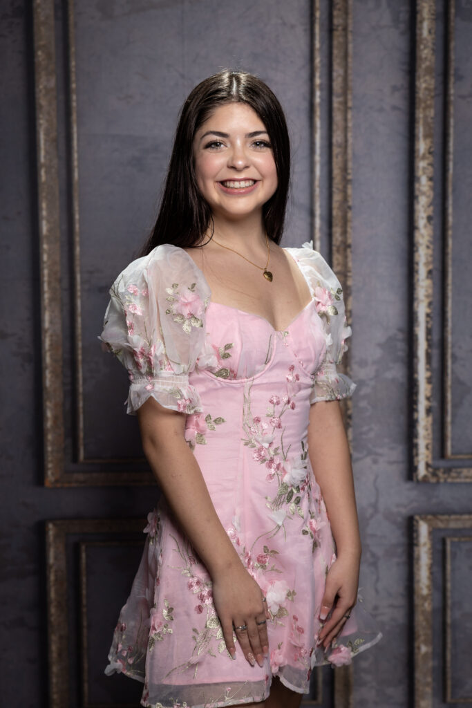 A girl wearing pink color designer dress, smiling at the camera