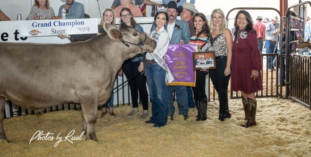 A group of people posing with a cow at a show.