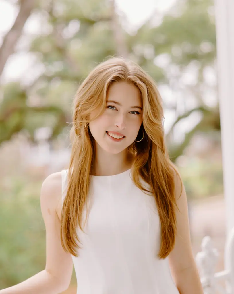 Woman smiling outdoors in a white dress.