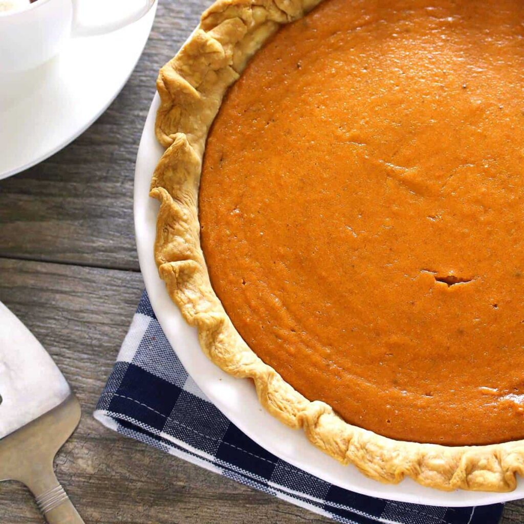 A pumpkin pie is sitting on a table next to a fork.
